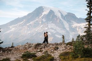 Hikers on a rocky mountain ridge with stunning views of Mount Rainier's snow-capped peaks in the background.