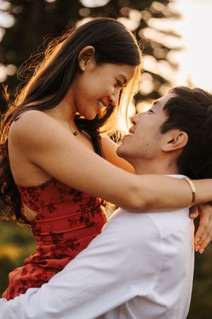 A romantic couple embraces at sunset, with the person in red dress spinning in their partner's arms in golden light.