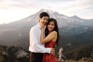 A couple embraces against a scenic mountain landscape with snow-capped peaks in the background.