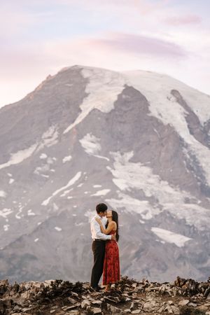 A couple embraces against a backdrop of Mount Rainier's snowy peaks during a romantic mountain engagement session.