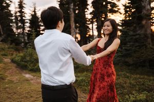 Couple in white and red outfits dances together in a forest setting during golden hour.