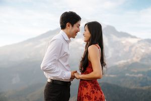 A couple shares romantic moments against a mountain backdrop while wearing a white shirt and red dress.