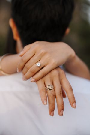 Close up of hands wearing two elegant diamond rings against a white dress background.