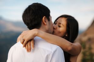 A couple shares an intimate embrace and kiss with mountains visible in the blurred background during golden hour.