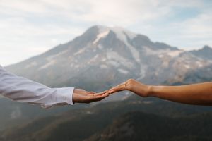 Two hands reach out to each other in a compassionate gesture against a backdrop of misty mountains at sunrise.