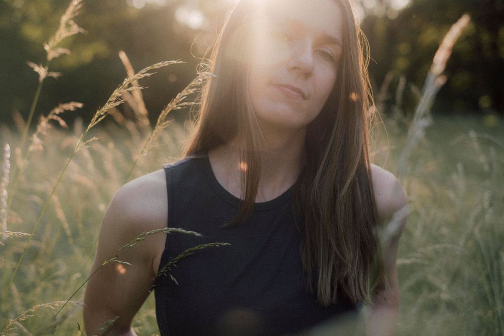 Person in dark sleeveless top walks through golden grass field at sunset.
