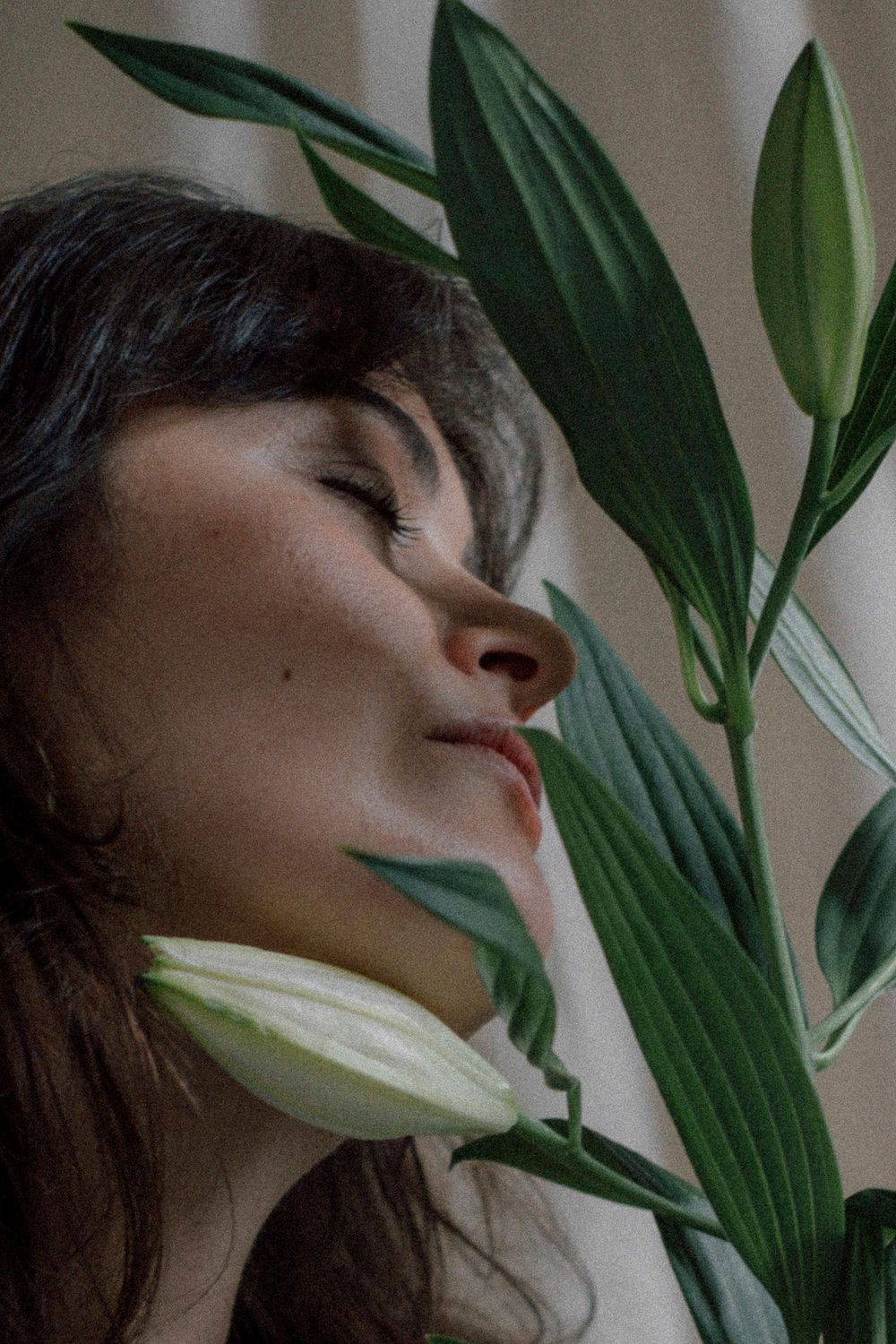 A person rests with their head tilted backwards against a backdrop of green tropical leaves in a creative portrait.
