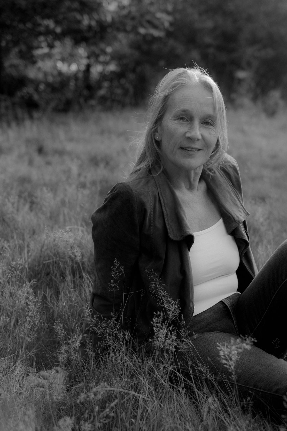 A series of black and white portraits showing someone reclining in tall grass wearing a black jacket and white top.