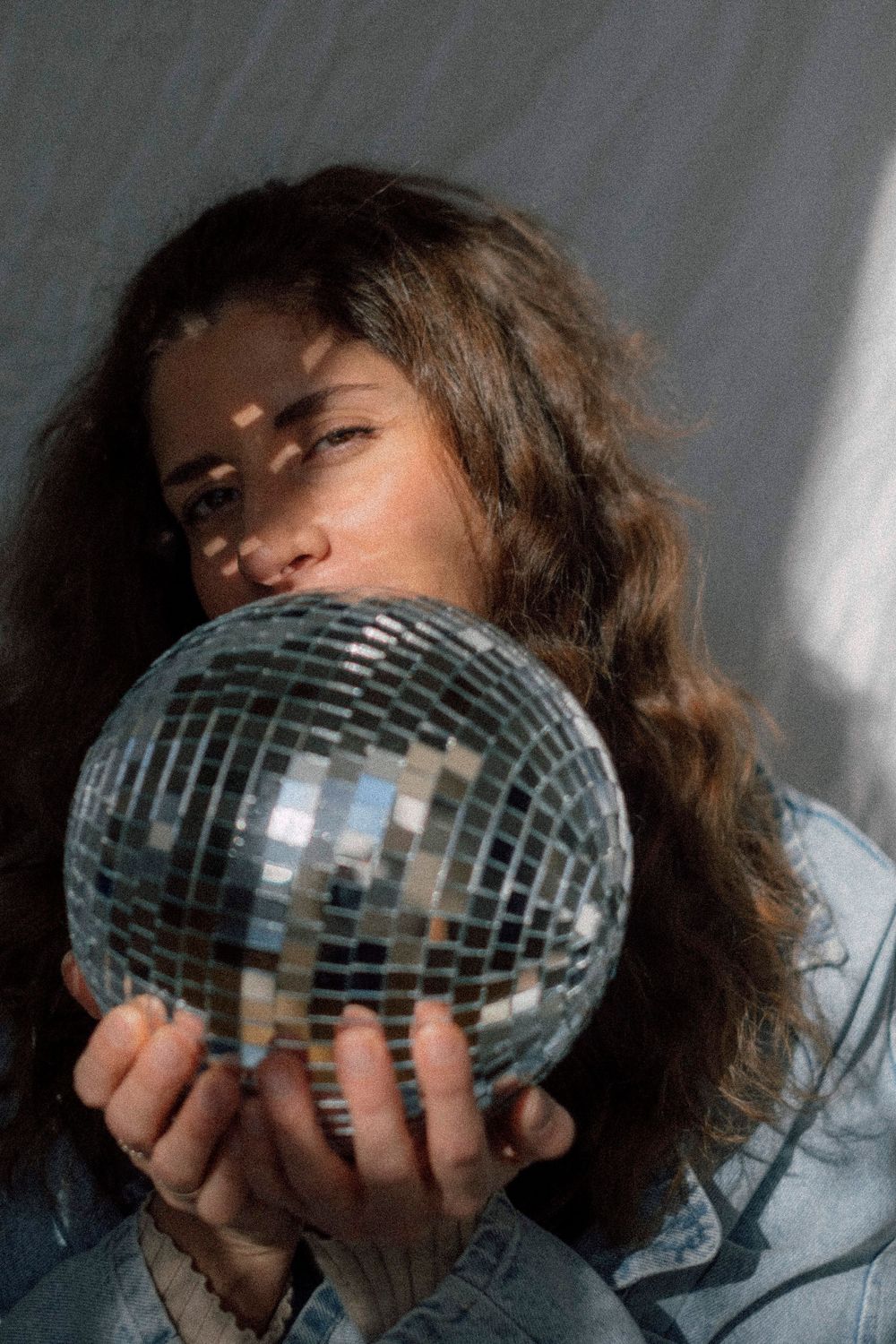 A person in denim holding and peeking behind a silver disco ball in a sequence of artful portraits.