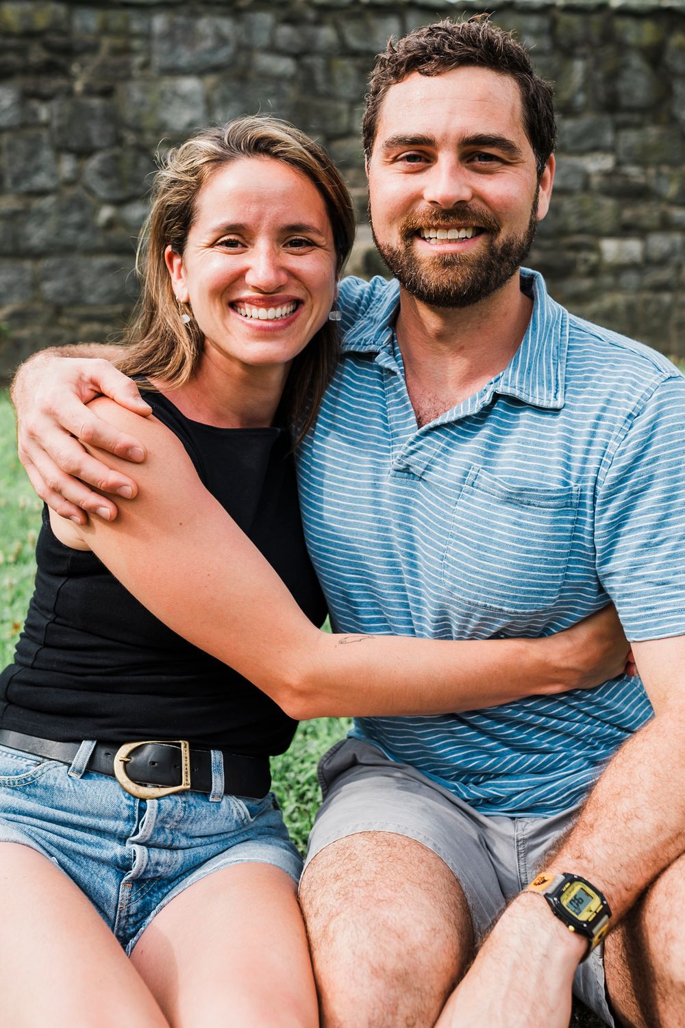 A couple relaxes together on stone steps while wearing casual summer outfits and denim.