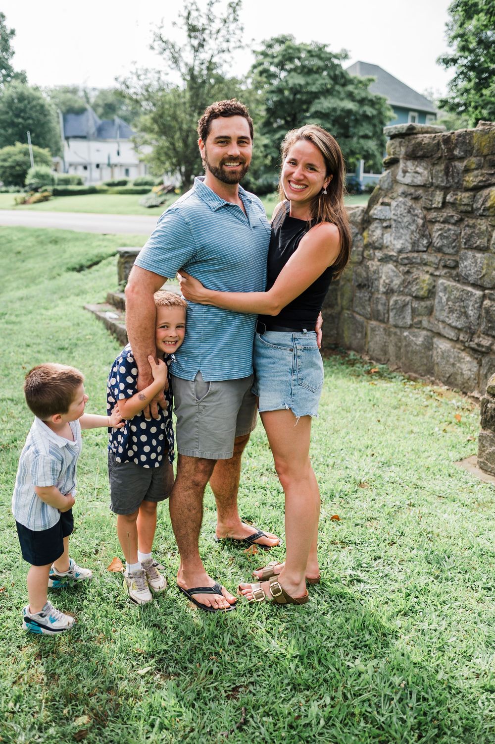 A family stands together on a green lawn near a stone wall on a sunny summer day.