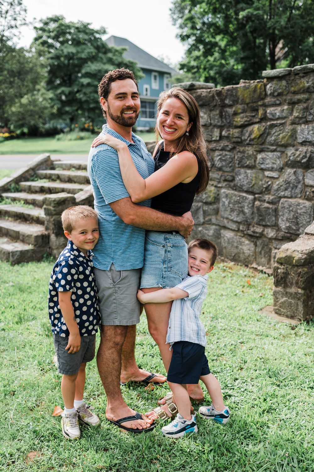 A happy family shares tender moments together by a stone wall while enjoying the outdoors on a sunny day.