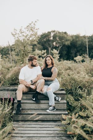 A couple sitting close together on rustic wooden steps having an intimate conversation amidst natural foliage.