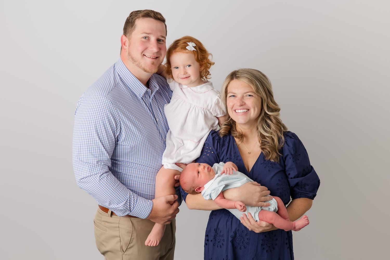 Family portrait against white background wearing coordinated navy blue and gray outfits.