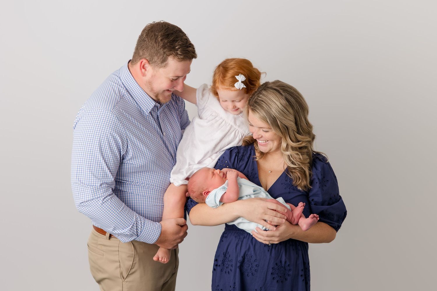Couple in grey and navy blue outfits share tender moments with their newborn baby in a lifestyle photography session.