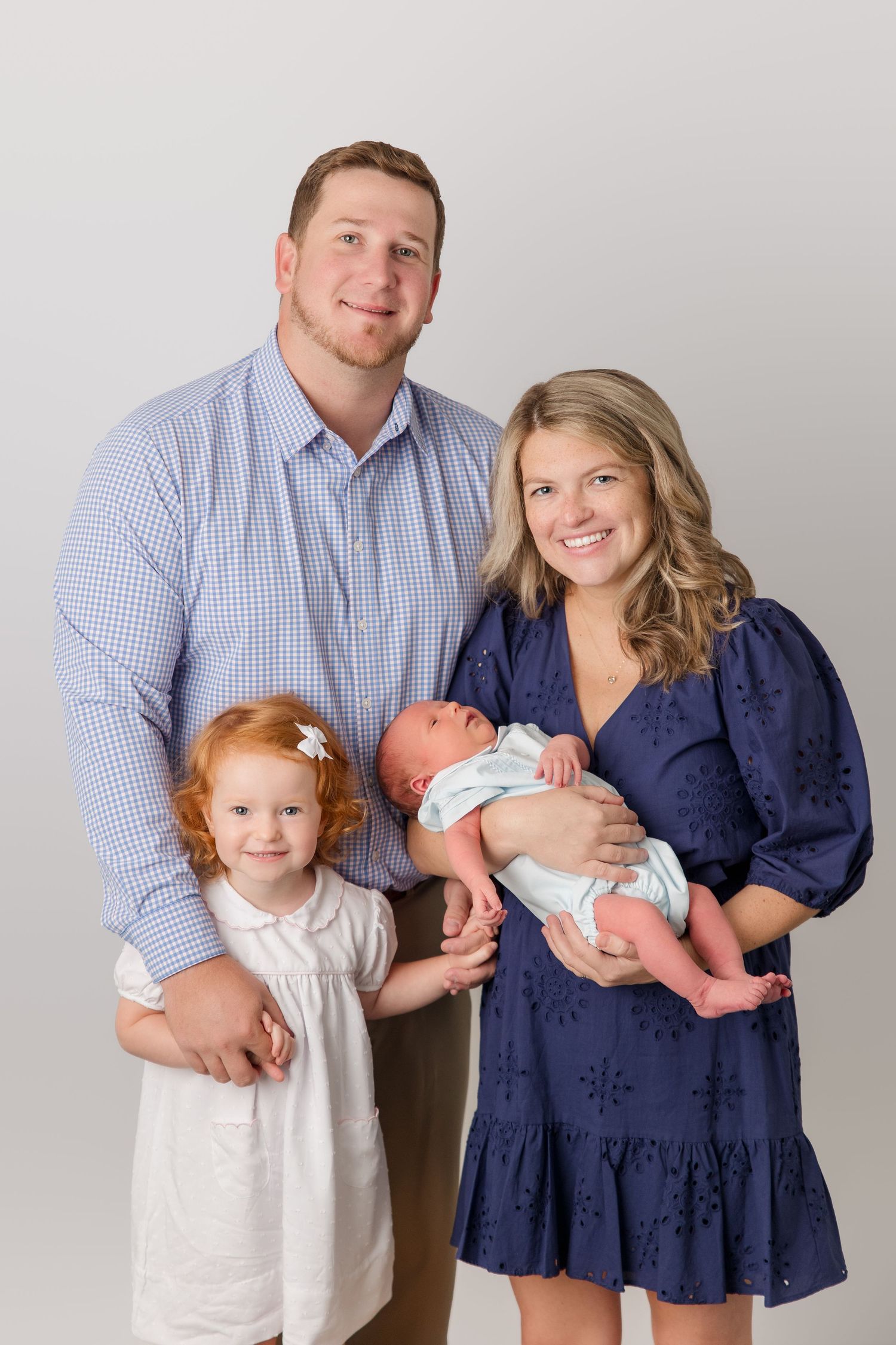 A family portrait series in casual attire against a neutral background with a baby and toddler.