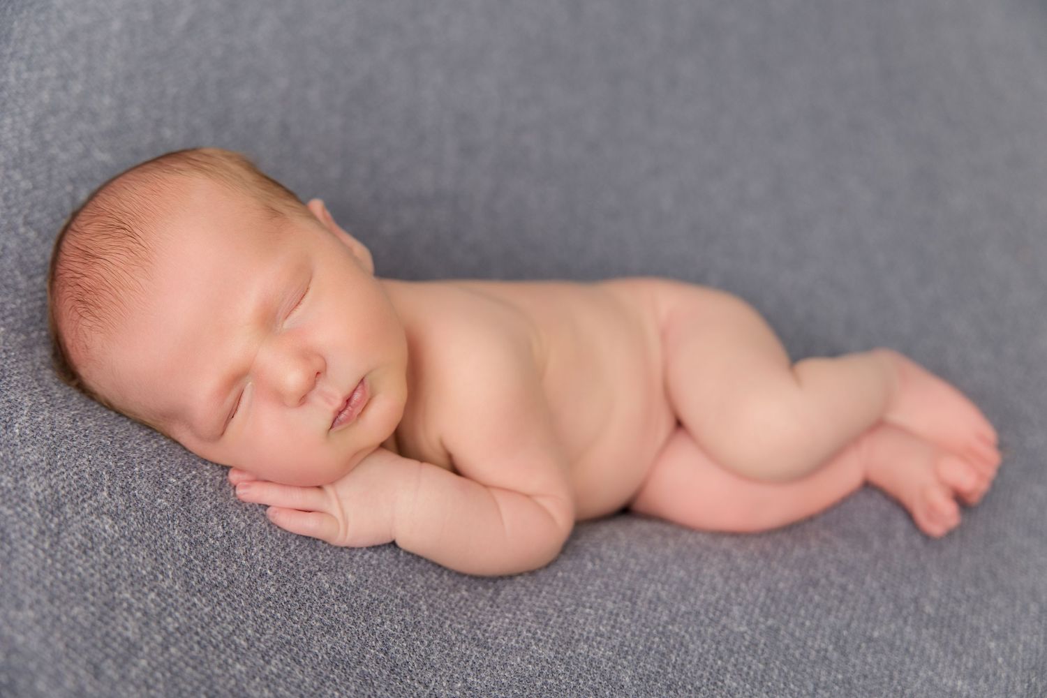 Peaceful sleeping newborn baby in natural pose on grey studio backdrop during professional photography session.
