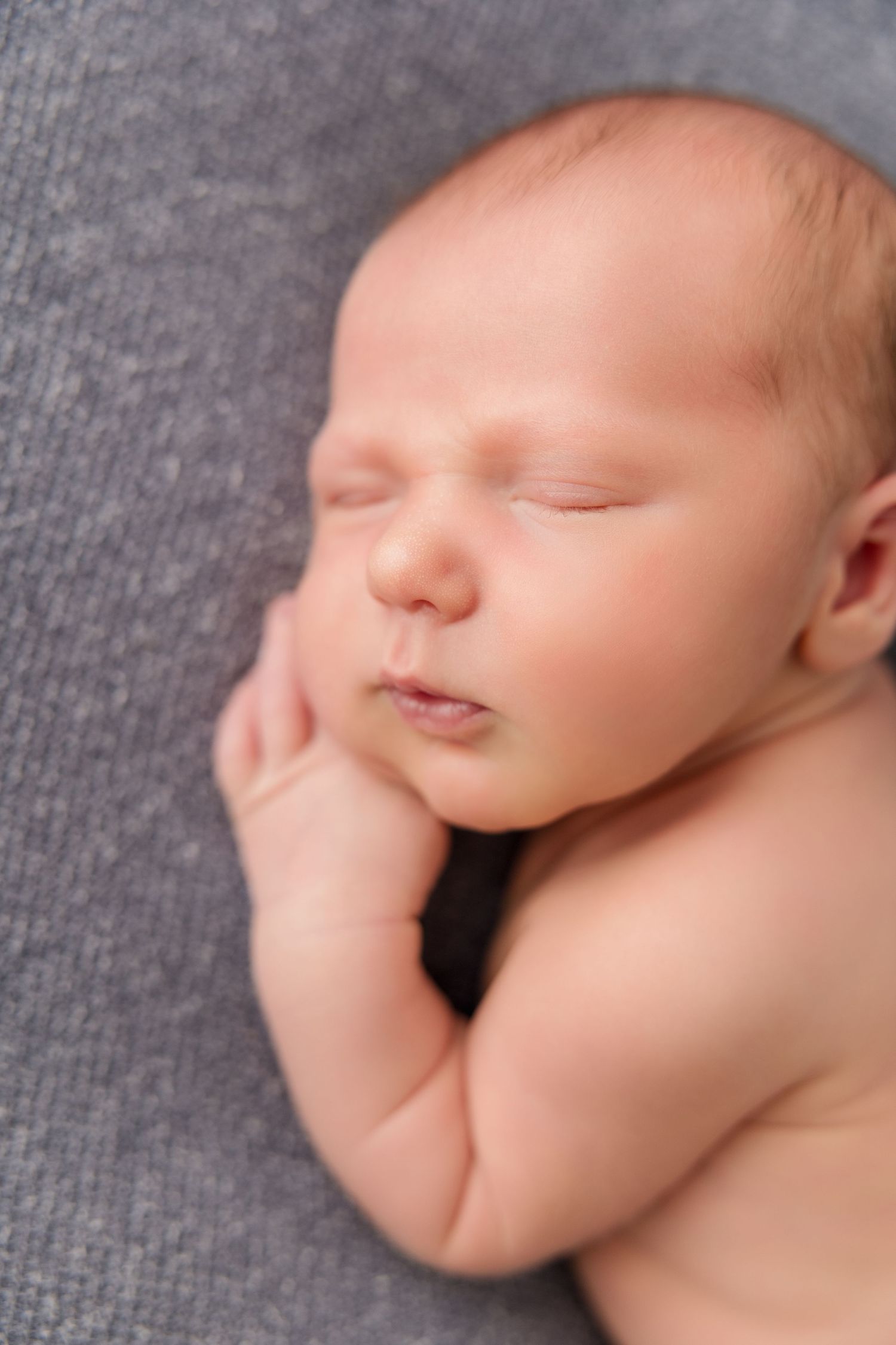 Close up profile view of sleeping newborn baby on gray textured backdrop.