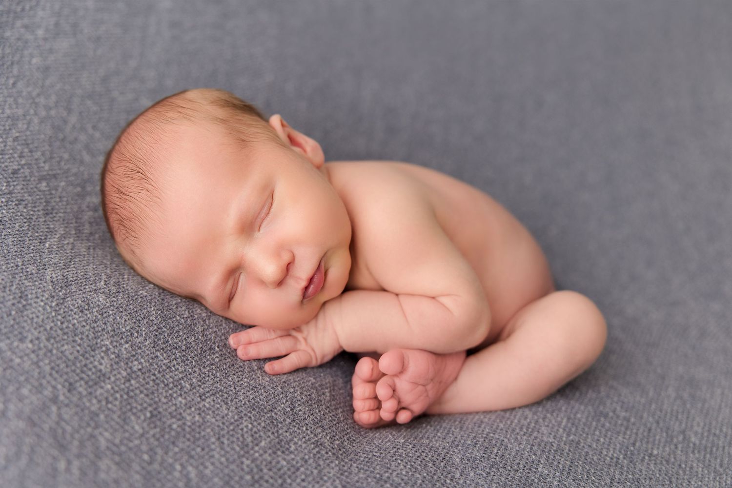 Peaceful sleeping newborn baby in gentle natural lighting on gray fabric background.
