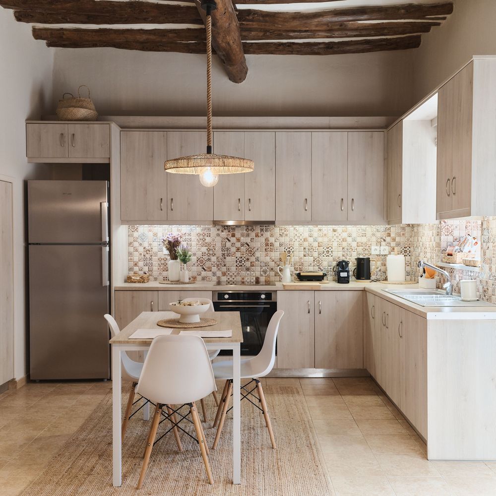 Modern rustic kitchen with white cabinets, patterned tile backsplash, exposed wooden beams, and small dining area.