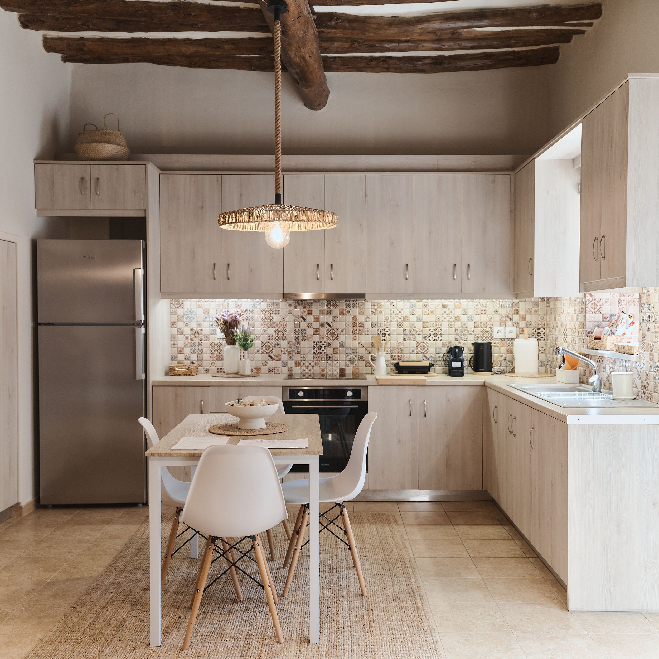 Modern rustic kitchen with white cabinets, patterned tile backsplash, exposed wooden beams, and small dining area.