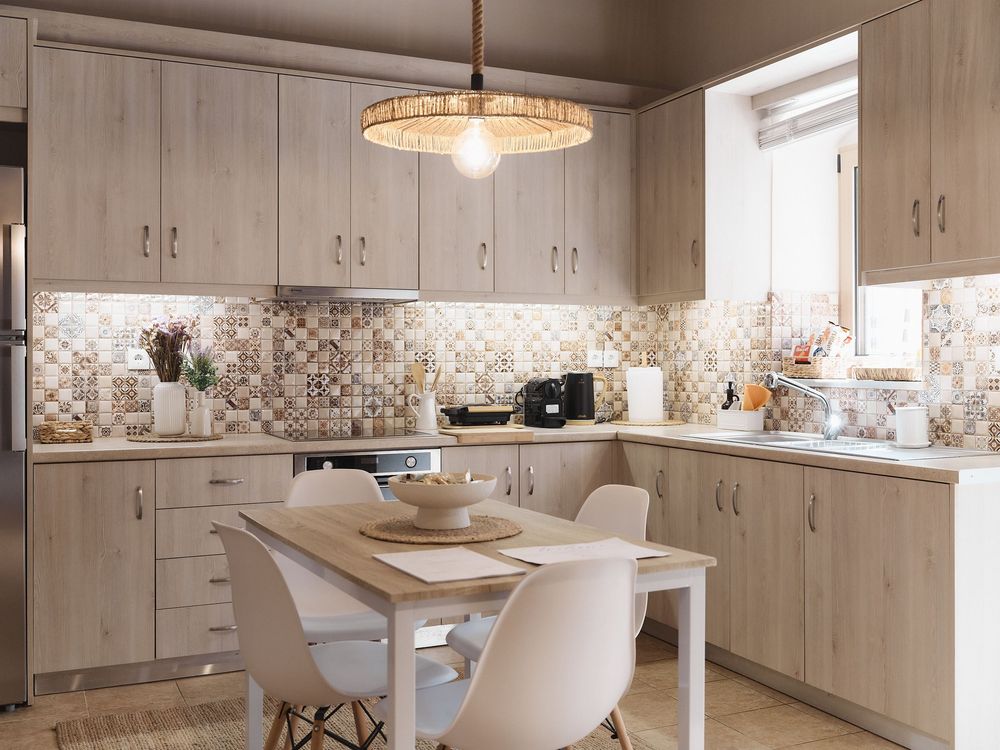 Modern kitchen interior with light wood cabinets, quartz countertops and circular chandelier over dining area.