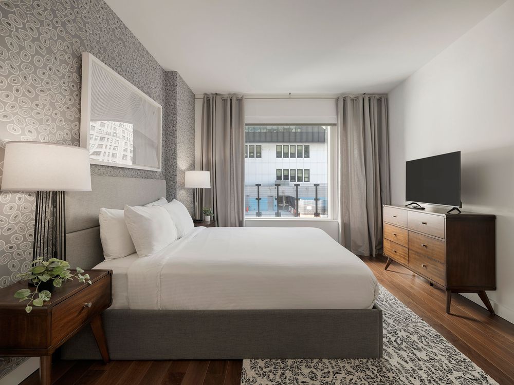 Contemporary bedroom design with textured wallpaper, wooden headboard, and natural lighting from city windows.