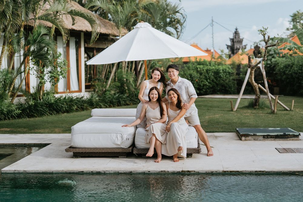 Friends gathered on a poolside lounger under a white umbrella at a tropical resort.