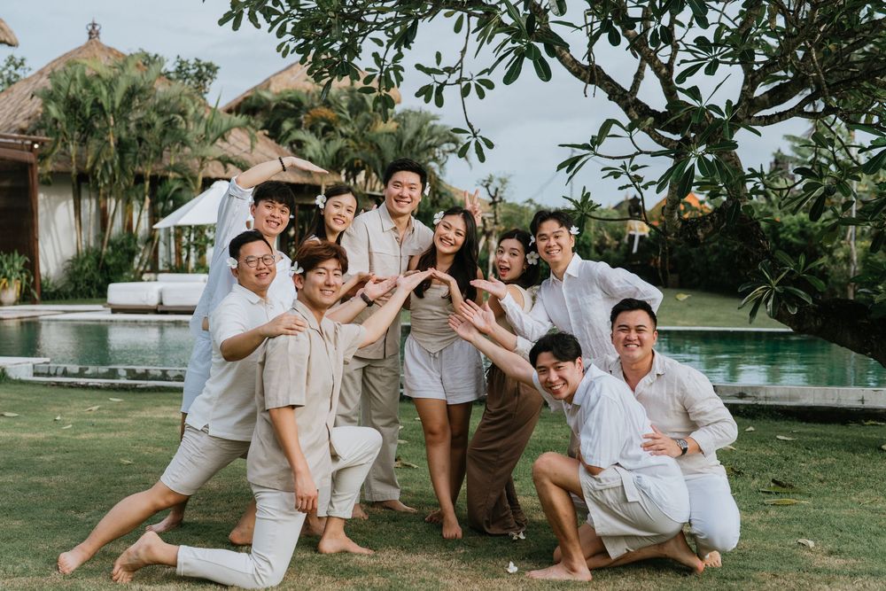 Playful group photo session on grass with everyone wearing coordinated white and beige outfits.