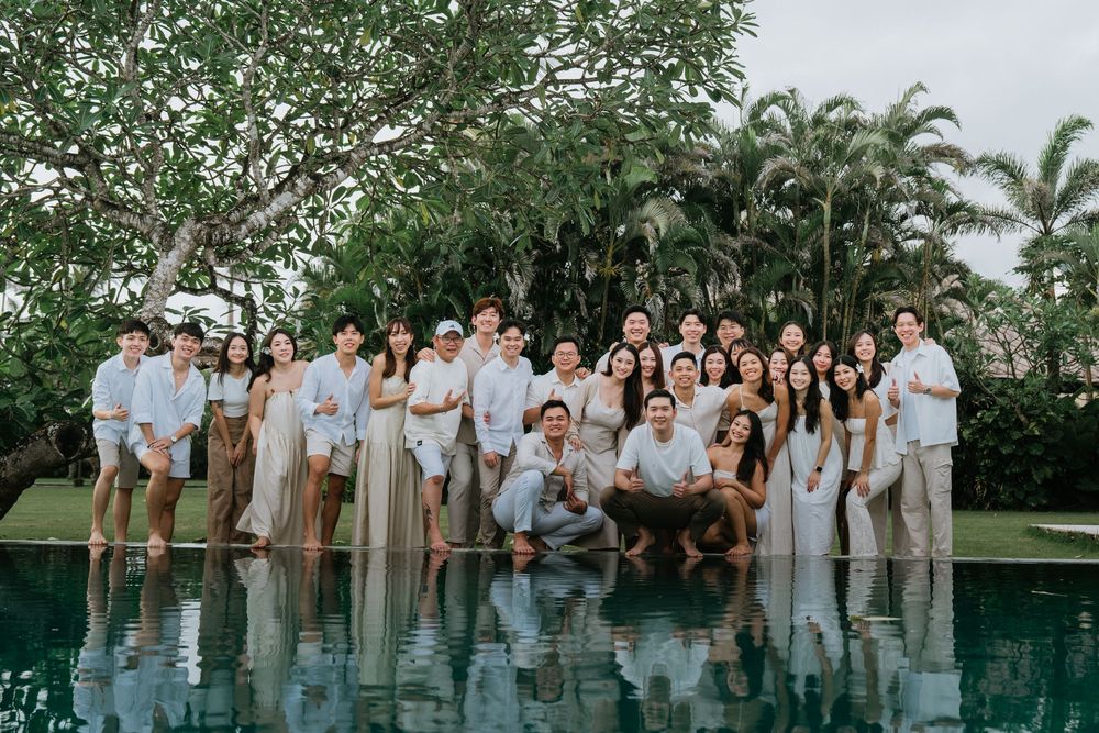Large group photo of people in coordinated white and beige outfits posing by an infinity pool.