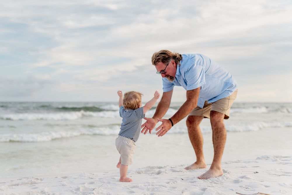 Two people playing and dancing together on a white sandy beach with ocean waves in the background.