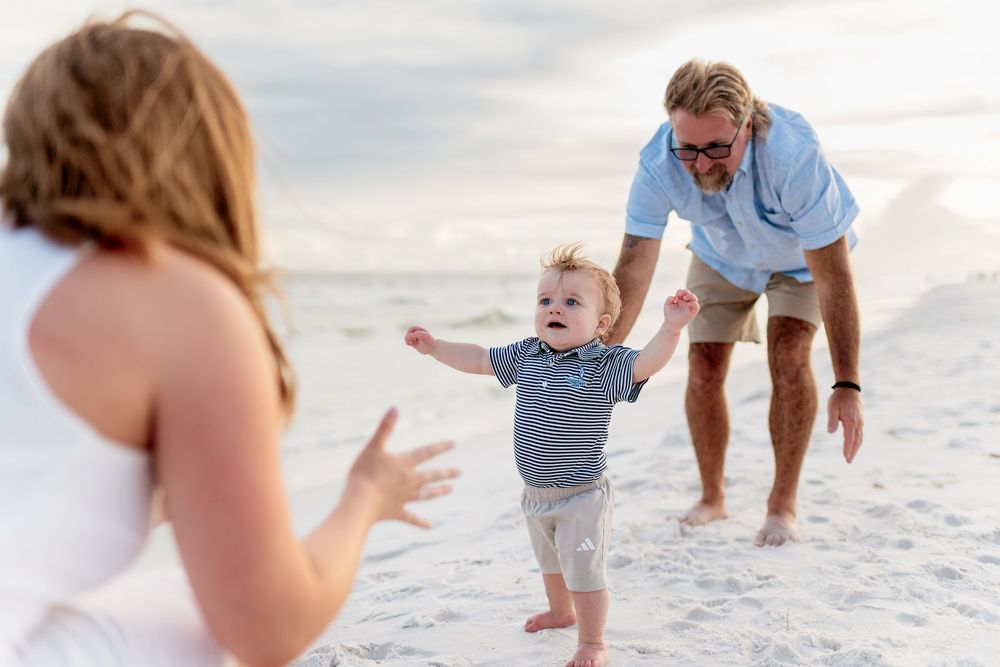 Family walking and playing together on a white sandy beach during sunset with ocean waves in background.