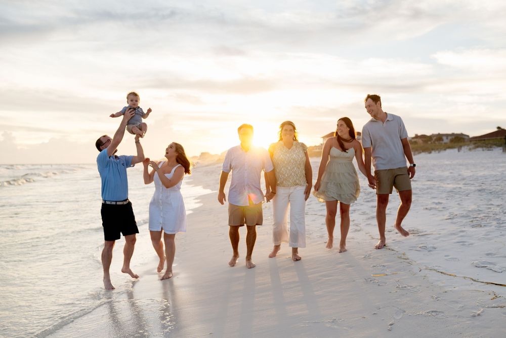 Family group walking together along a beach at sunset with golden light illuminating their silhouettes.