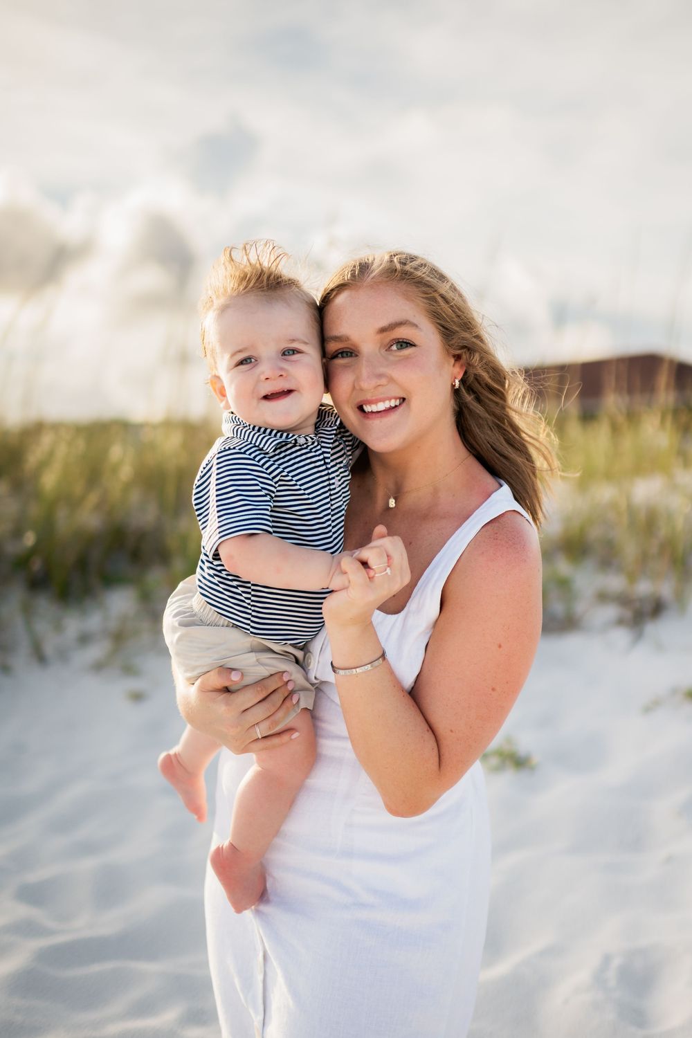 A tender moment between parent and child on a sunny beach with white sand dunes in the background.