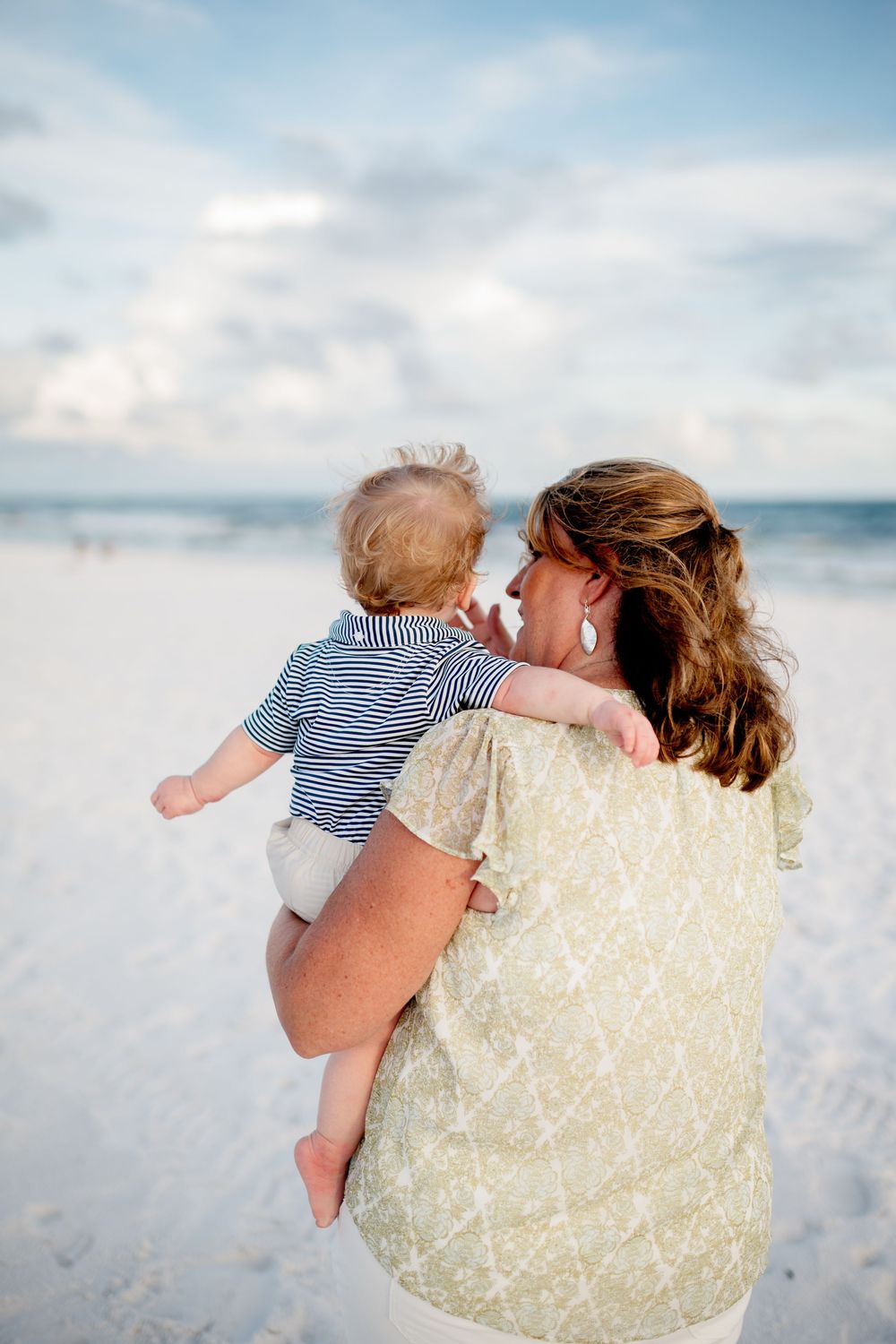 A tender moment between parent and child against a dreamy beach backdrop with soft clouds and ocean waves.
