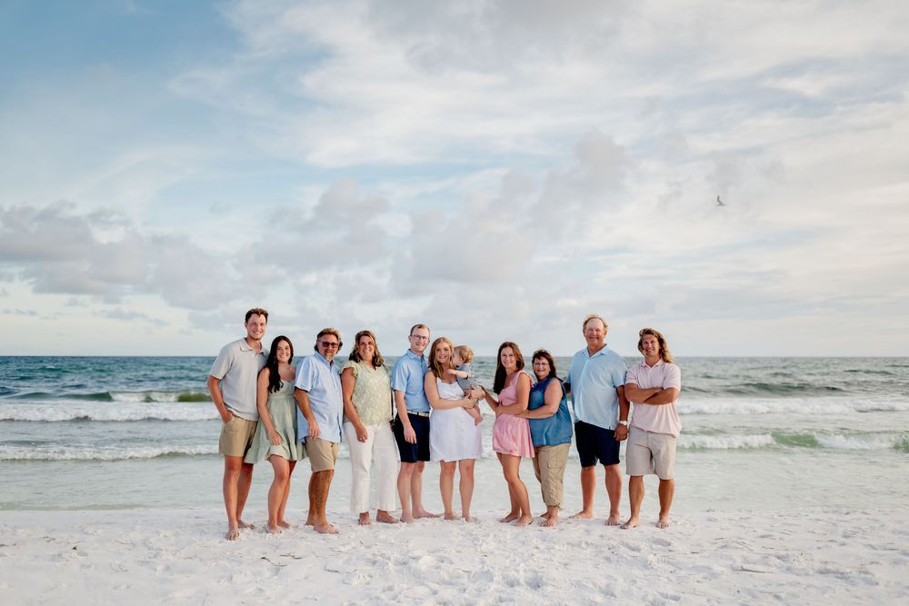 A group of people stand together in casual beachwear along the shoreline at sunset with waves crashing behind them.