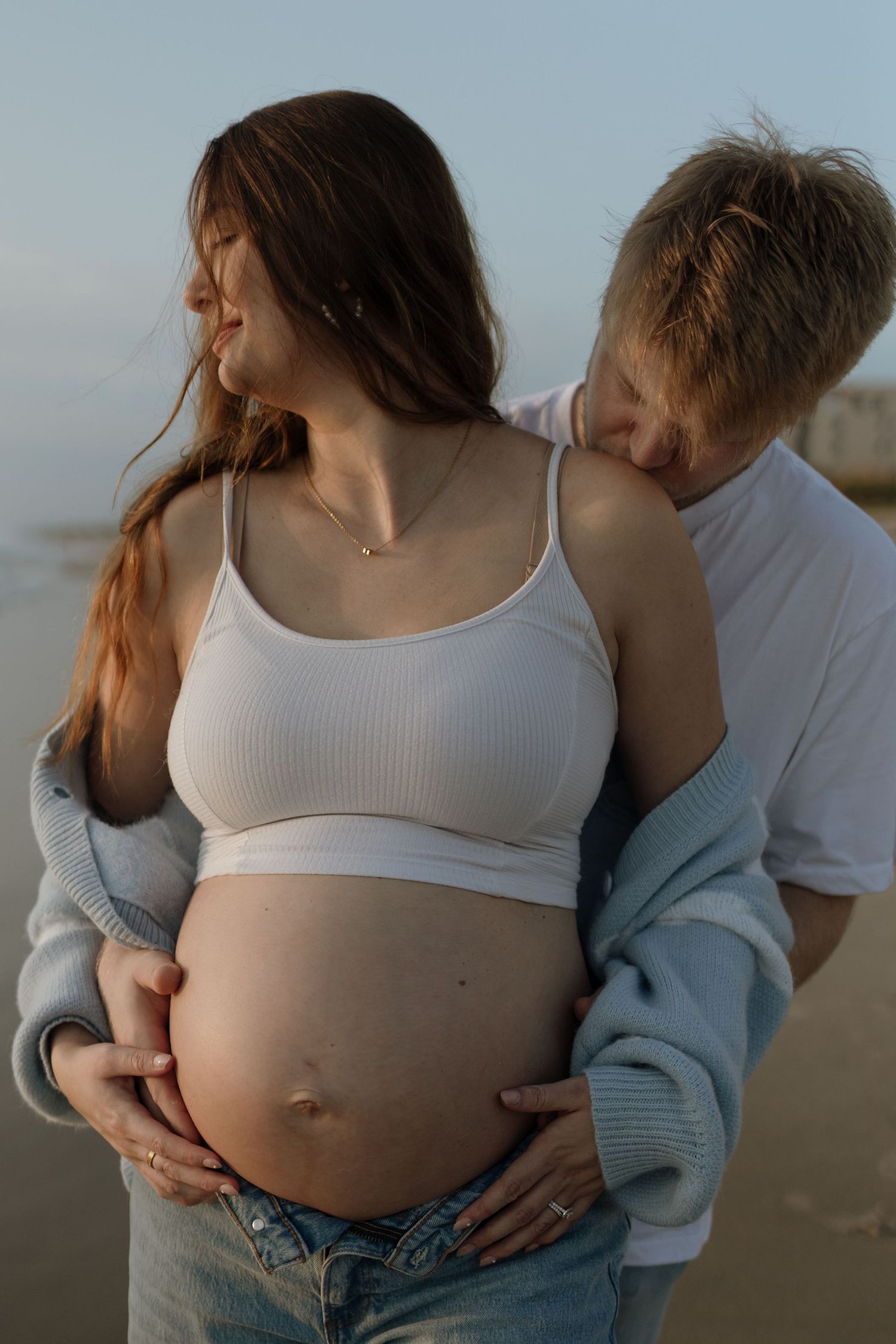 Intimate maternity photos on beach showing couple embracing pregnant belly. Sunrise golden hour on the Space Coast, Florida.