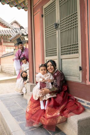 Family wearing traditional Korean hanbok poses along historic palace corridor.