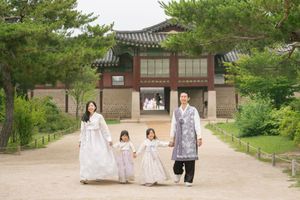 People in traditional Korean dress walking along garden path near palace buildings.