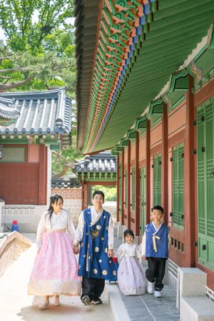 People in traditional Korean hanbok walking through palace corridors with colorful painted beams.