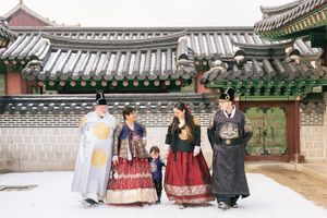 Group wearing colorful hanbok poses in front of traditional Korean palace architecture.