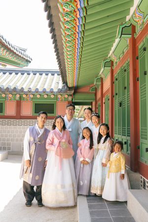 Group portrait in colorful hanbok dress under ornate green and red painted palace roof.