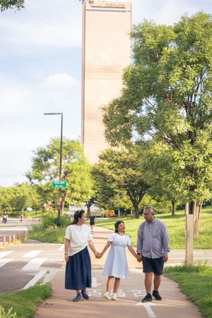 A couple strolls together through a park-like setting with tall buildings visible in the background.
