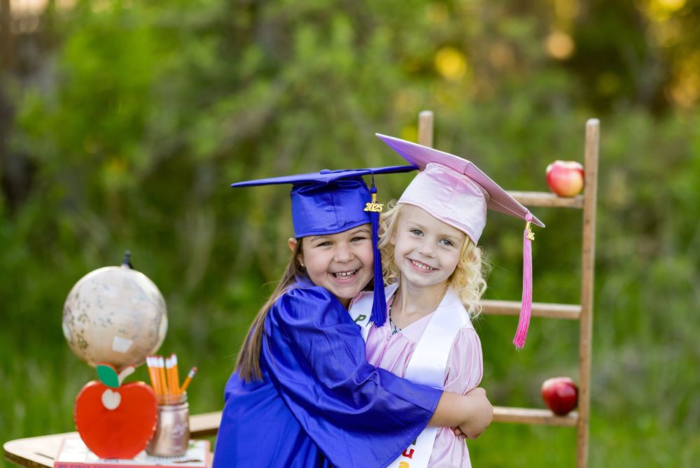 Children in graduation gowns laugh and play together at an outdoor celebration event.