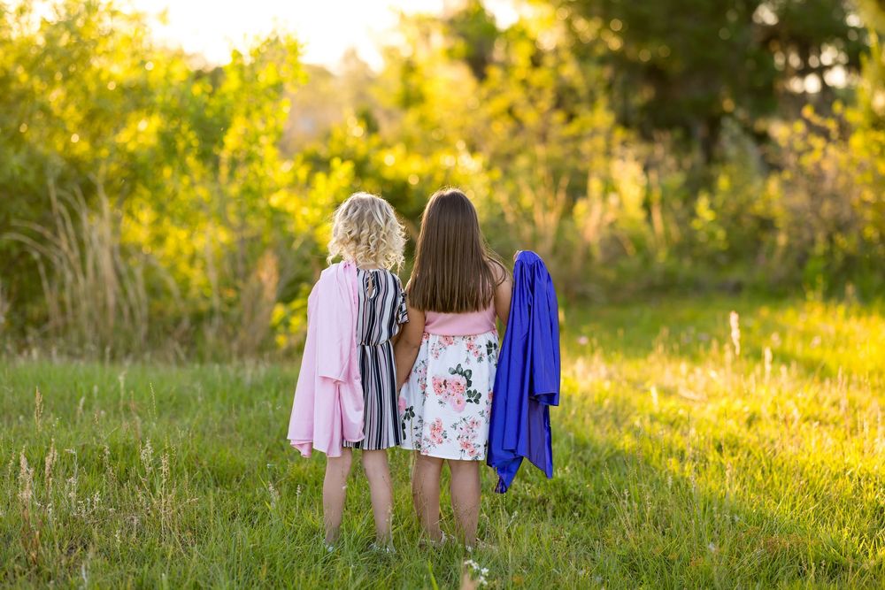 Three outfits in soft pastel colors laid out on grass during golden hour sunset lighting.