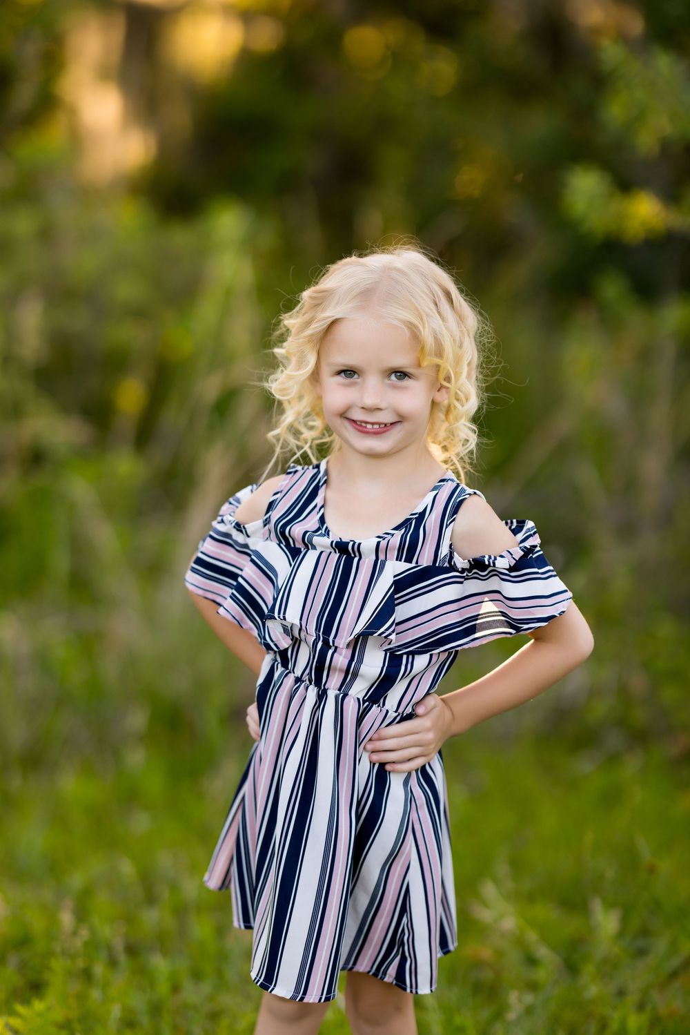 Child wearing a navy and white striped dress plays joyfully in a lush green outdoor setting.