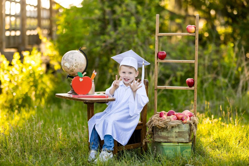 Small child in white shirt sitting in grass during sunset picking apples from basket in summer orchard setting.