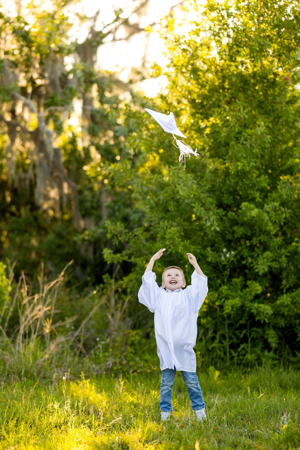 Child playing and jumping with joy in a sunlit meadow with green bushes and grass in the background.