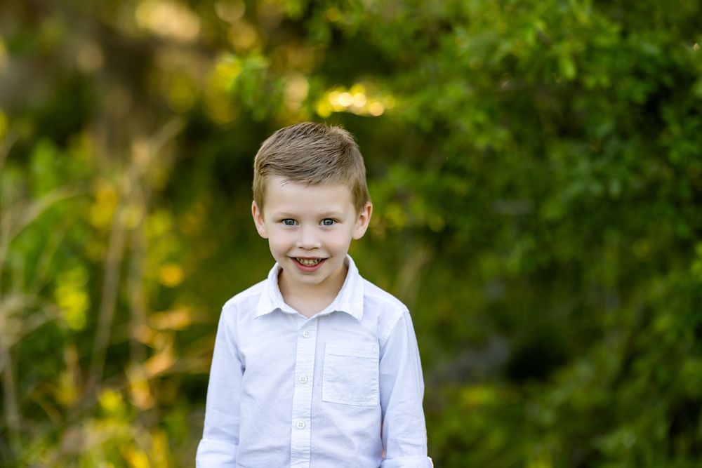 Family photo session in front of lush green trees and foliage during golden hour in a natural outdoor setting.
