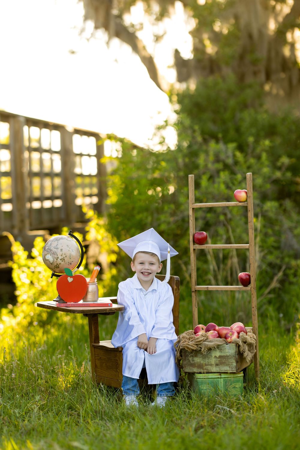 A decorative display with chairs, tree stumps, and apples arranged in a sunny garden setting at golden hour.